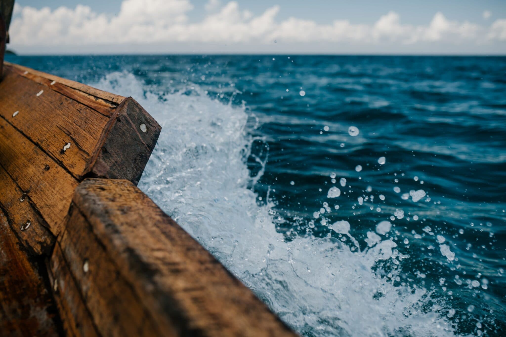 Waves crashing against the wooden bow of a boat on open water